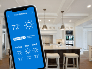 A smartphone shows a kitchen climate control app set at 72 degrees with sunny icons for three days, ensuring you keep warm. In the background is a modern kitchen featuring a large island, bar stools, pendant lights, and white cabinets.